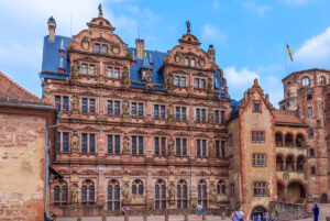 A view of the Renaissance Friedrichs wing, a fanciful building in red sandstone with a pair of curlicued gables at the top against a dark blue roof. There are niches on the three main floors of the facade with carved stone statues and a blue sky overhead.
